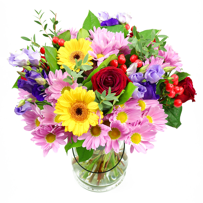 This abundant mixed bouquet is arranged in a clear glass vase, set against a white background that allows every colour and texture to take centre stage, much like a carefully styled display in a Chessington high street shop. At its heart, rich red roses with velvety petals spiral inward, creating a deep, romantic core to the design. Flanking them on either side, bright yellow gerbera daisies with distinctive dark brown-orange centres beam outward, their bold discs bringing a joyful, sunlit energy. Surrounding these focal blooms, clusters of soft pink and lilac daisies or chrysanthemums spread over the top of the vase, each bloom composed of numerous slim petals encircling a central yellow button; they lend a gentle, almost feathery fullness that balances the stronger shapes. Rising through and above these softer flowers, lisianthus in shades of purple and lavender contribute a touch of elegance, their bell-shaped blossoms and curving buds lending refined height and depth. Nestled among the petals, glossy red hypericum berries sit in neat clusters, adding pops of round, smooth texture that catch the light. A medley of greenery holds the bouquet together: broad, dark green leaves offer solidity and frame the brighter flowers, while slender, lighter-green sprigs weave in and out, suggesting a freshly gathered, garden-like charm reminiscent of the more peaceful corners of Chessington, away from the bustle of the theme park. The stems are clearly visible through the transparent vase, neatly trimmed and fanned in clear water, displaying the underlying structure that supports the generous dome of blooms above. Soft, even lighting enhances the vivid reds, yellows, purples, and pinks, creating an overall mood of warmth and celebration - an ideal gift to deliver across Chessington for birthdays, anniversaries, or simply to light up a friend's home near Hook or along Moor Lane.